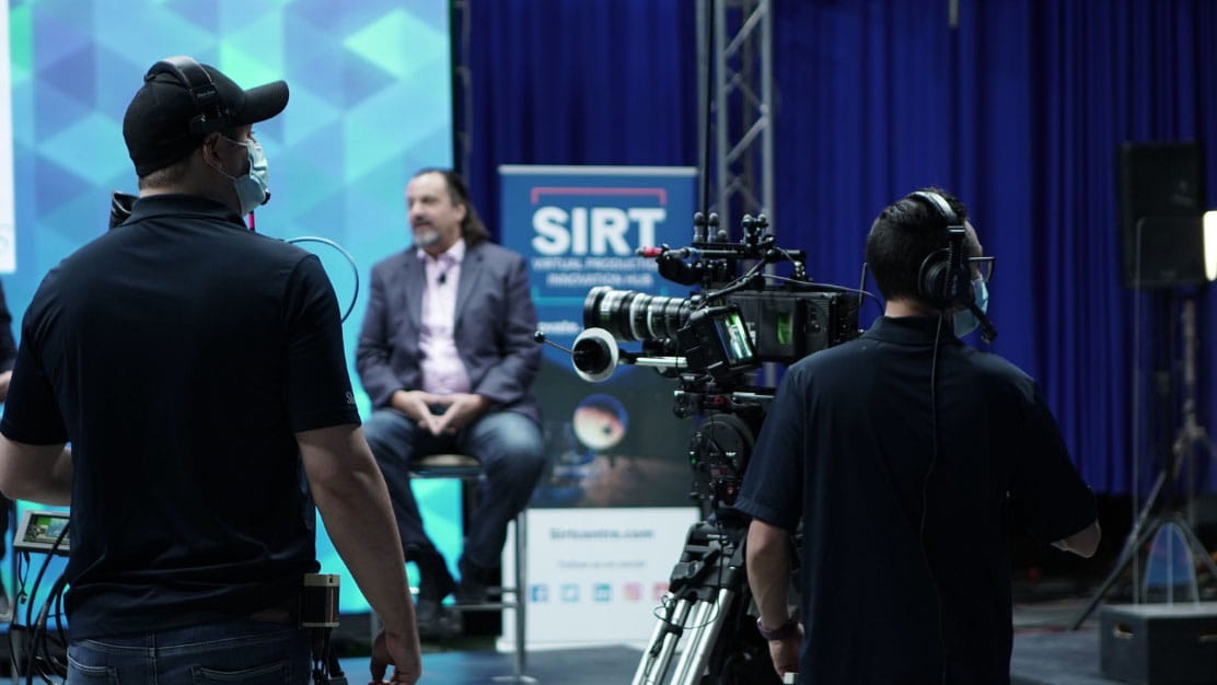 Two-person crew filming a subject on stage.