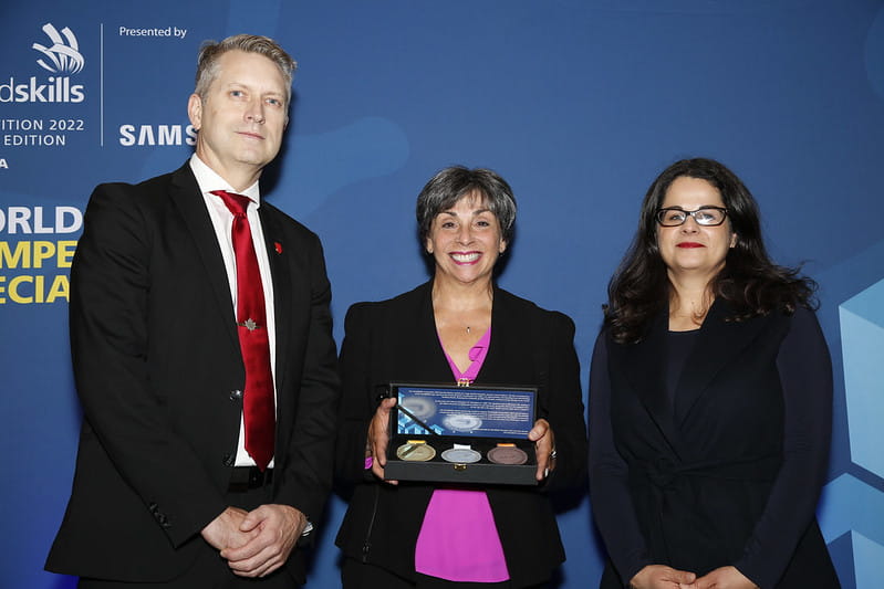 Carol Altilia, Sheridan's Provost and Vice-President, Academic, stands in between two Skills Canada officials and displays replica medals Sheridan received for hosting the WorldSkills Competition 2022 Special Edition's Industrial Mechanics event.