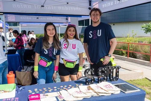 Three students wearing SSU t-shirts stand at a table under a tent