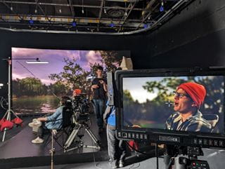 Two students sit in front of the LED screen in Sheridan's LED volume while a camera in the foreground shows what the viewer sees