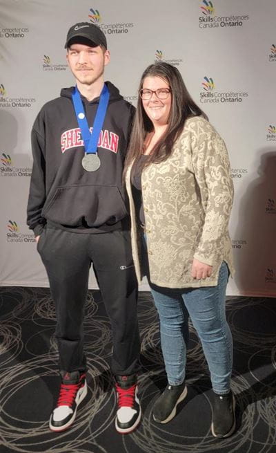 Welding student Lucas Blackwood stands with his mentor Carly Myers while wearing his Skills Ontario silver medal
