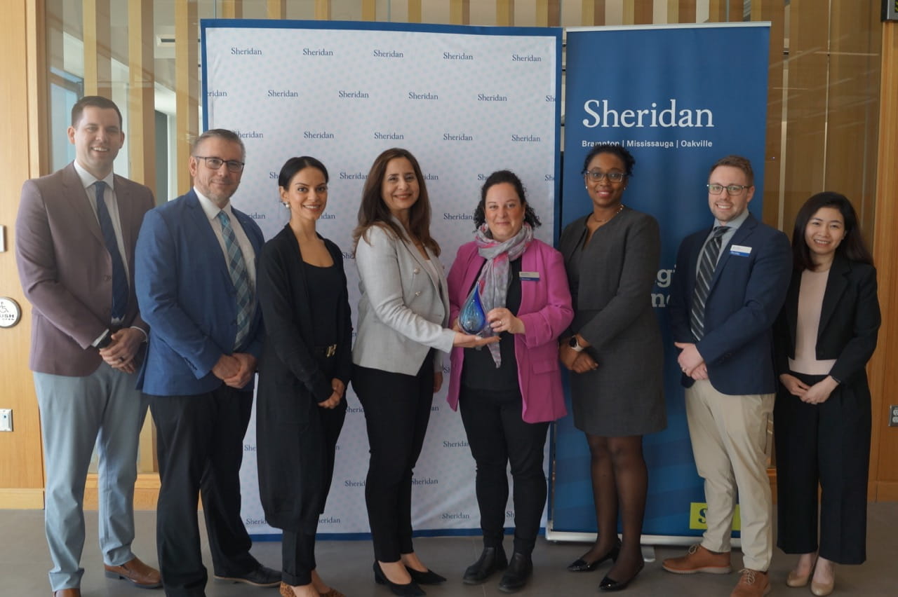 Representatives of Sheridan and the Peel District School Board stand side by side for a group photo in front of Sheridan signage