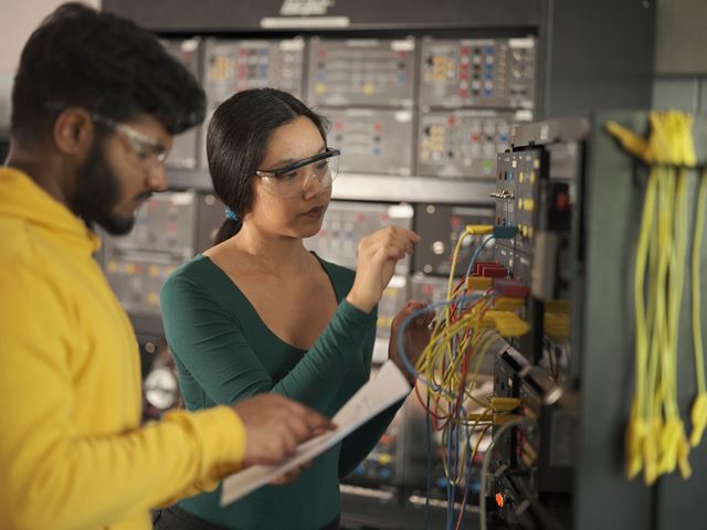 Two electrical engineering students examine the wiring on a panel