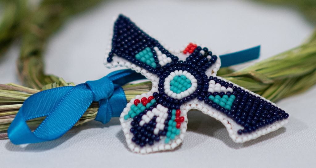 Close up image of beaded thunderbird pin with sweetgrass braid