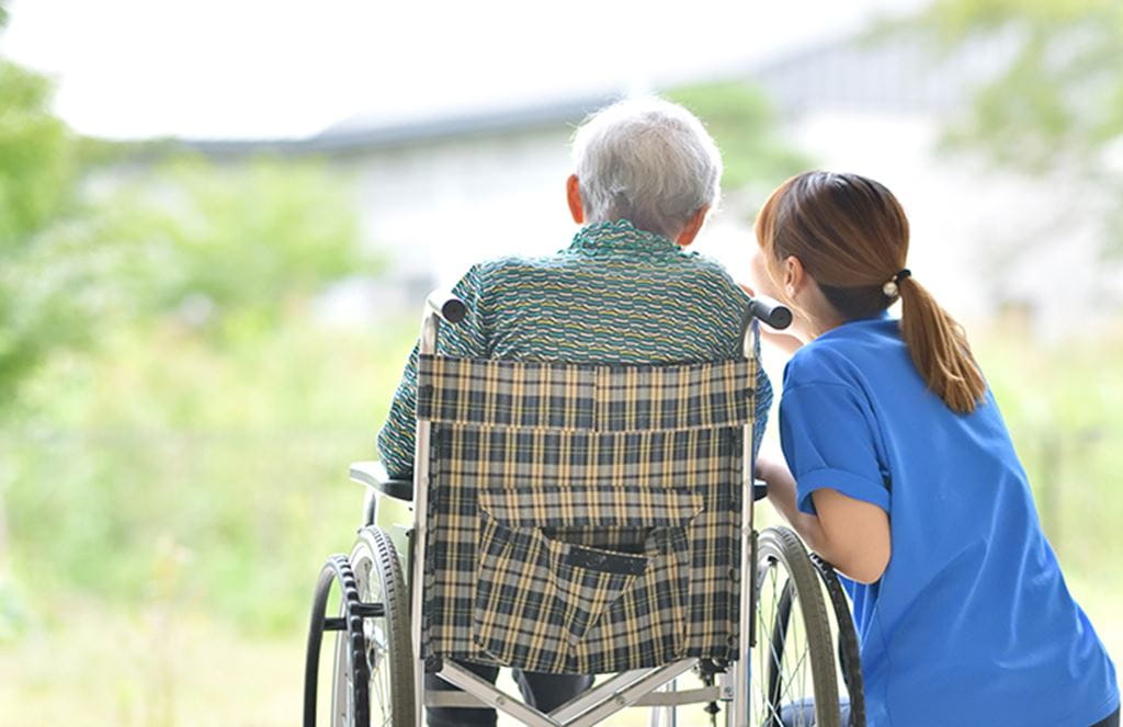 A personal support worker crouches next to an older adult seated in a wheelchair