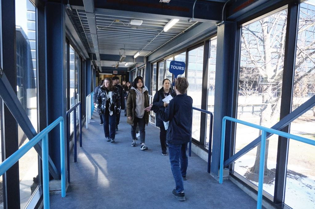 A tour guide leads a group through a hallway of one of Sheridan's campuses