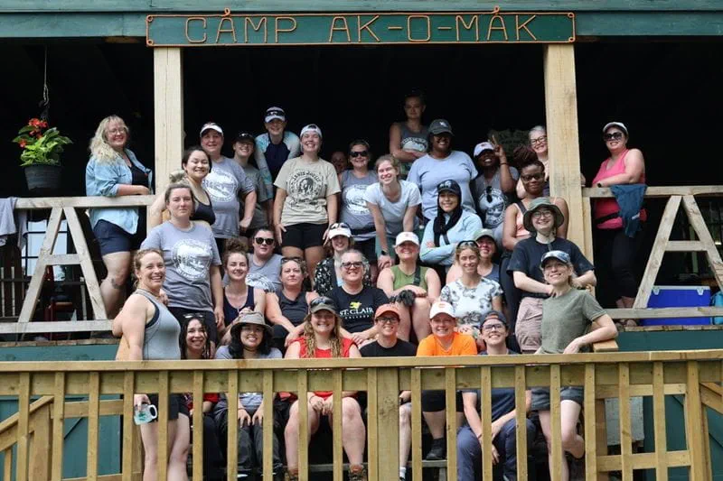 Journeywomen and female skilled trades students gather for a photo under the Camp Ak-O-Mak sign