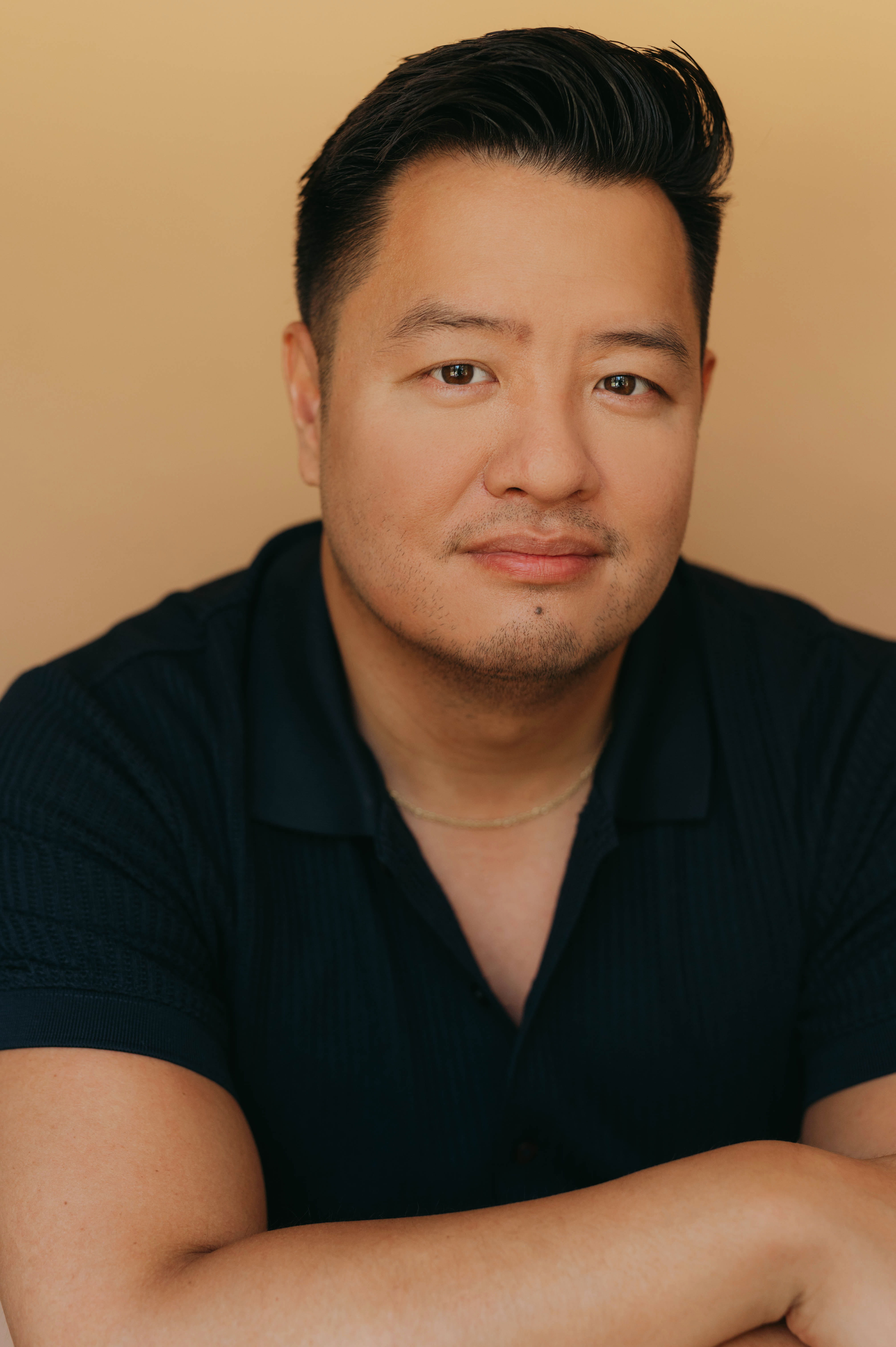 A headshot of Kevin Wong wearing a dark blue button-down shirt in front of an orange background