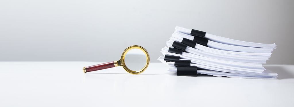 A magnifying glass sits on its edge next to a stack of documents