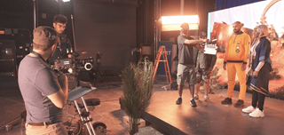 Two camera people prepare for a shot of actors on a stage in front of an LED volume screen