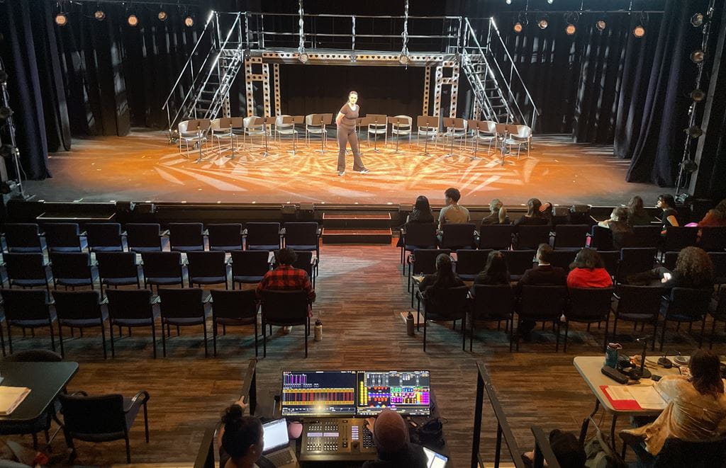 A performer takes centre stage while classmates sit in the audience seats to watch