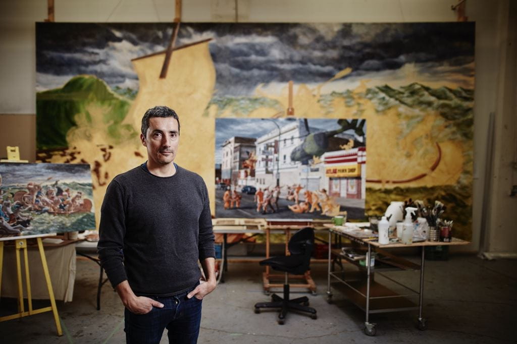 Kent Monkman stands in the foreground with some of his art behind him