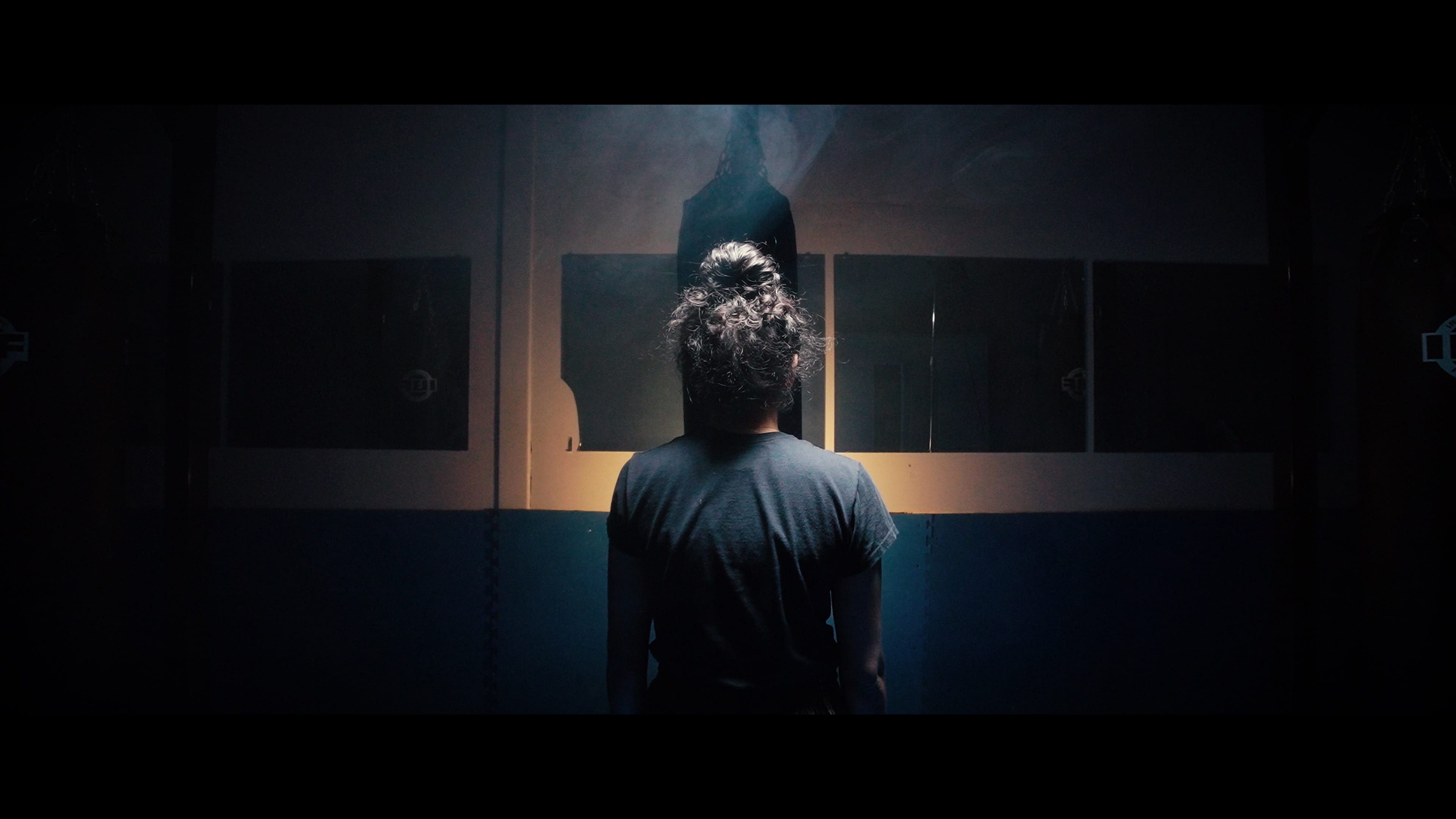 Muay Thai martial artist Navreet Chadee sits and faces a punching bag in a dark gym