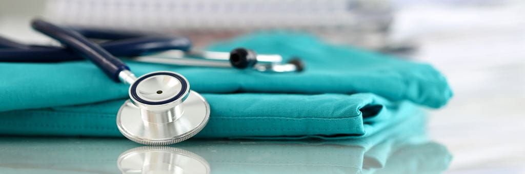A folded pair of teal nursing scrubs and stethoscope on a table