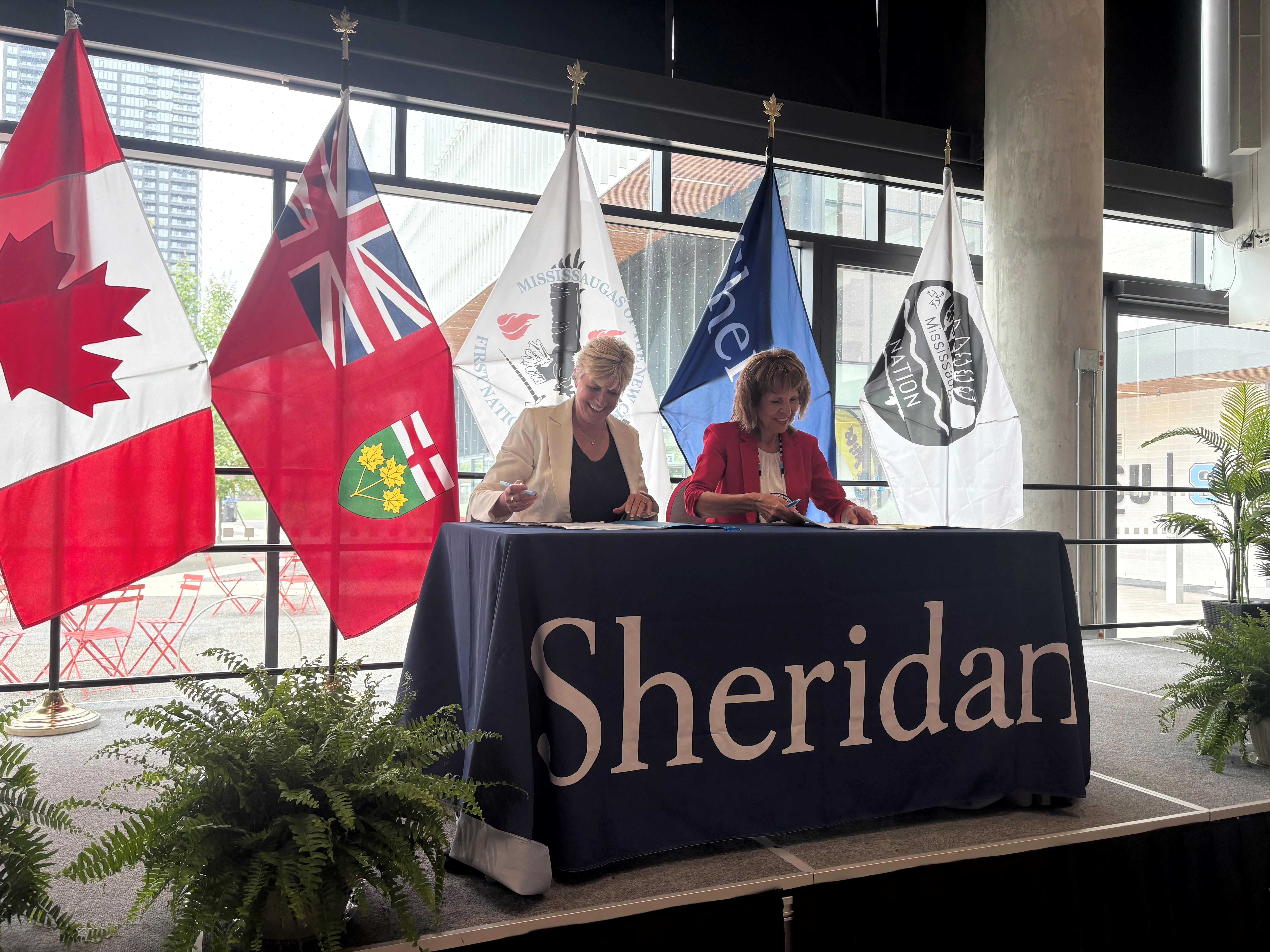 Mary Vaughan and Chief Claire Sault sit at a table and sign a memorandum of understanding document.