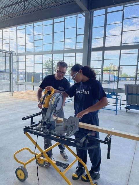 An instructor and a student work on a project on a machine.