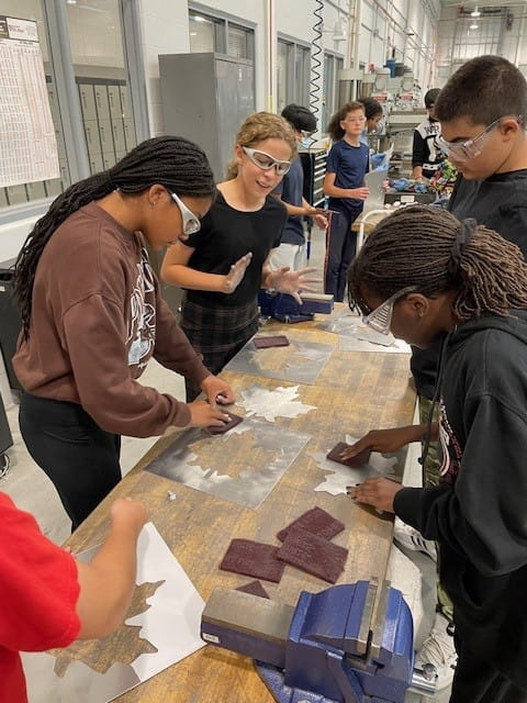 A group of students gather around a table and work on a project.