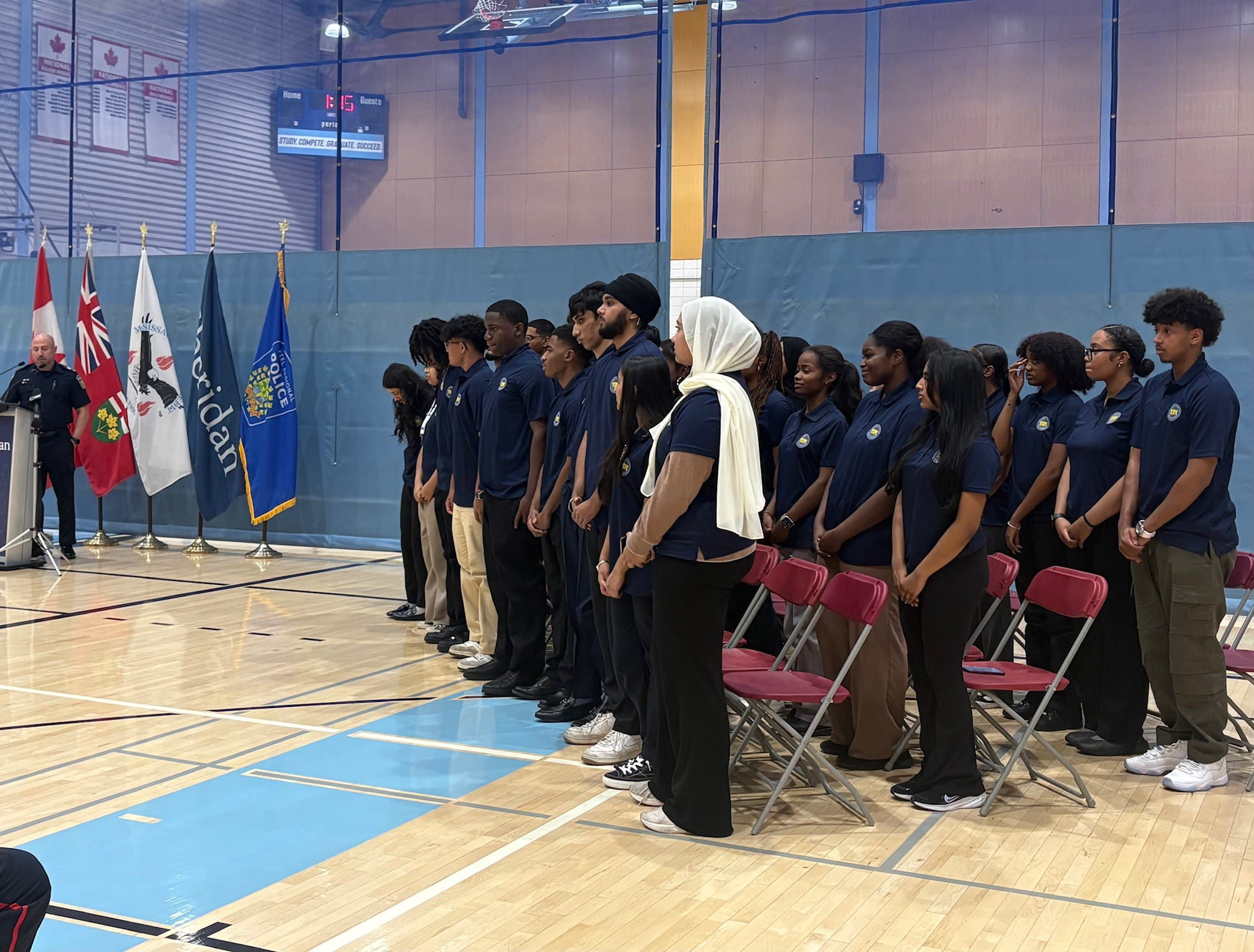 The group of YIPI students stand in front of their chairs as they are welcomed by a police sargeant.