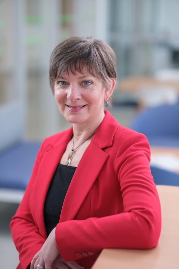 Vicki Mowat smiles at the camera while wearing a red blazer in an open space