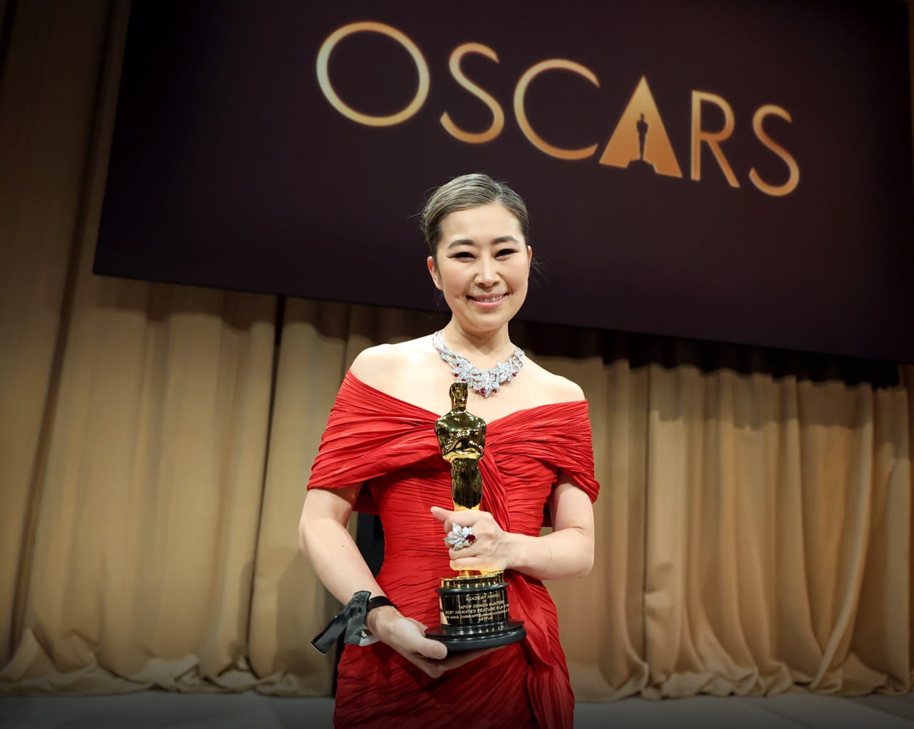 Sheridan Animation graduate Maggie Kang is pictured in a red dress holding her Academy Award trophy with an Oscars banner in the background