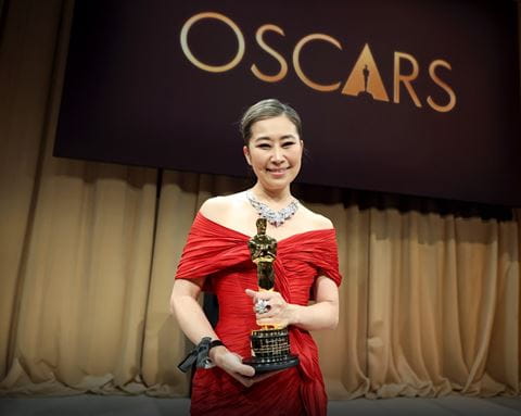 Sheridan Animation graduate Maggie Kang is pictured in a red dress holding her Academy Award trophy with an Oscars banner in the background