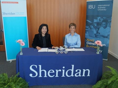 Presidents from Sheridan and International Business University sit at a table to sign documents.