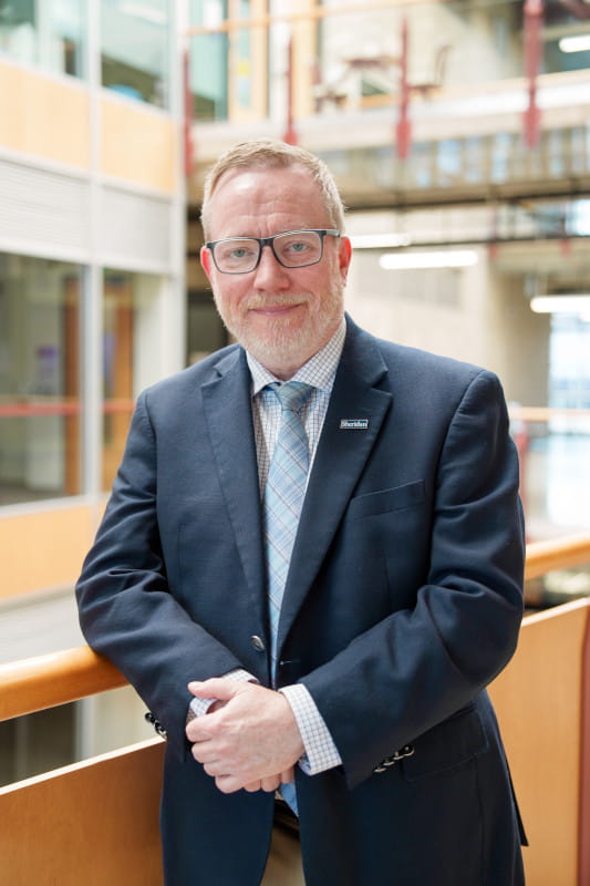 Sean McNabney is pictured in a suit and tie standing inside one of Sheridan's buildings