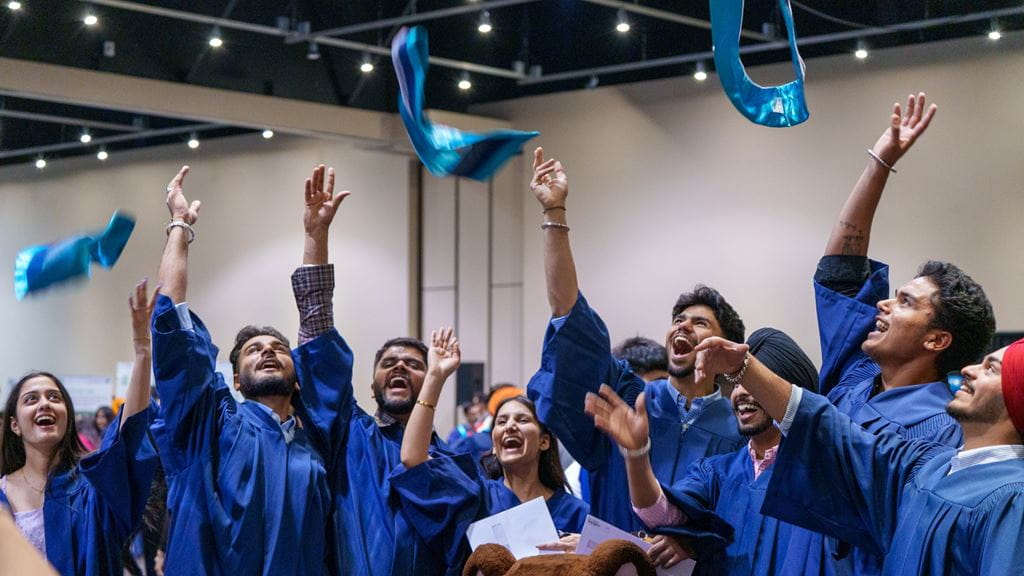 Students wearing blue graduation robes throw blue collars in the air at convocation.