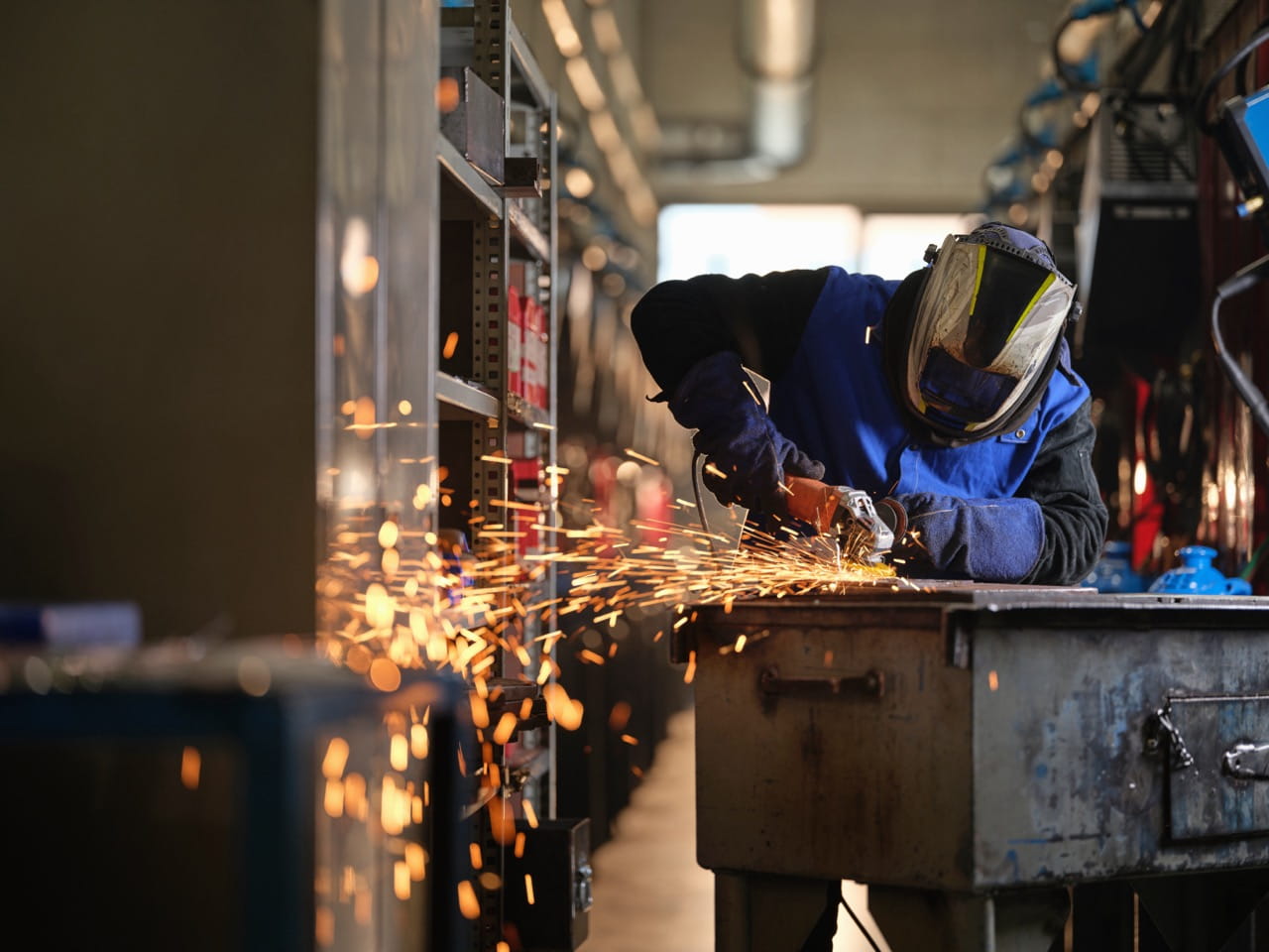 Sparks fly as a person stands at a table operating a metal grinder