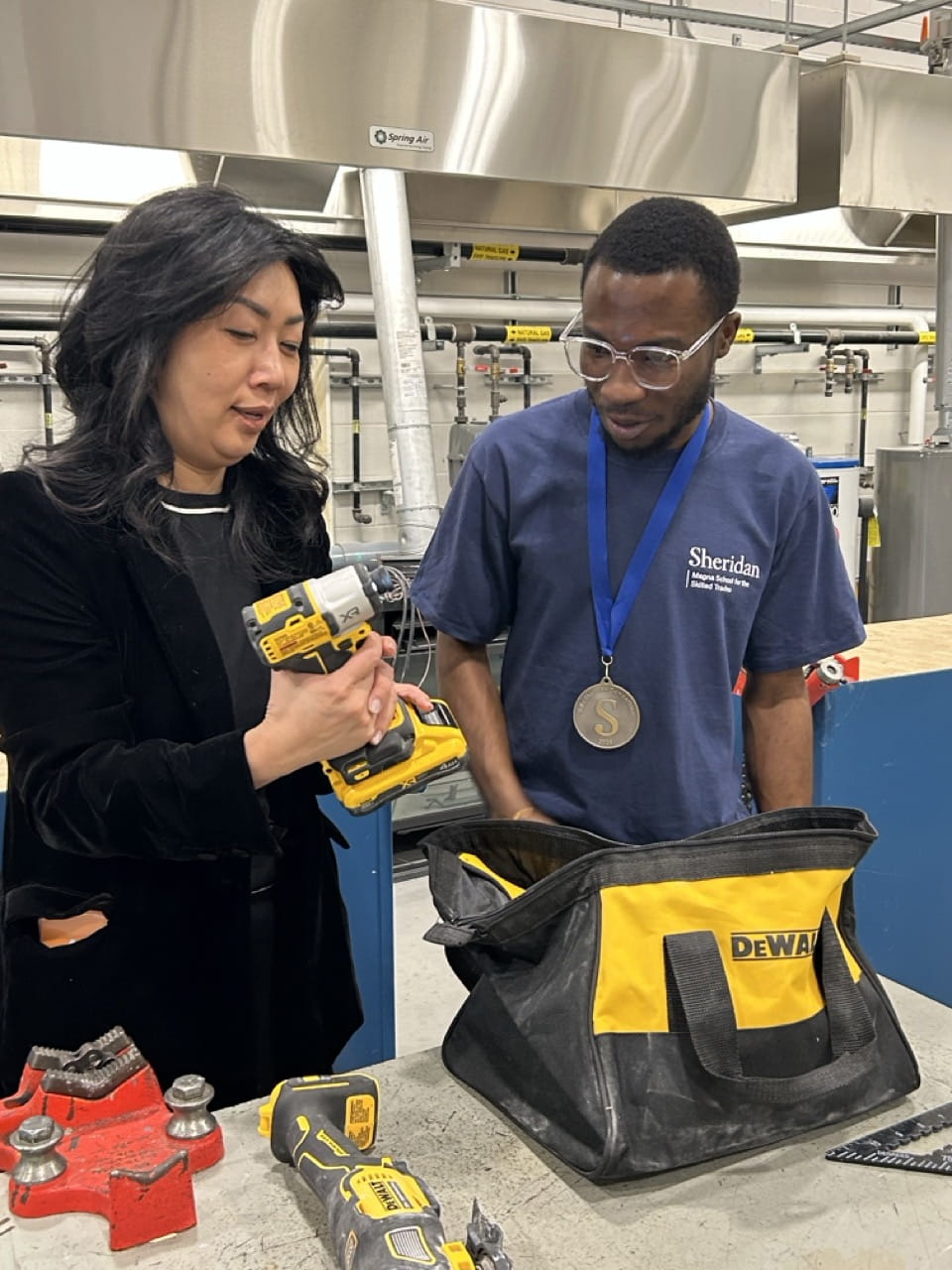 Sheridan President Dr. Cindy Gouveia examines a power tool alongside a Sheridan student