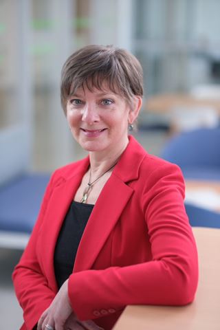 Vicki Mowat smiles at the camera while wearing a red blazer in an open space