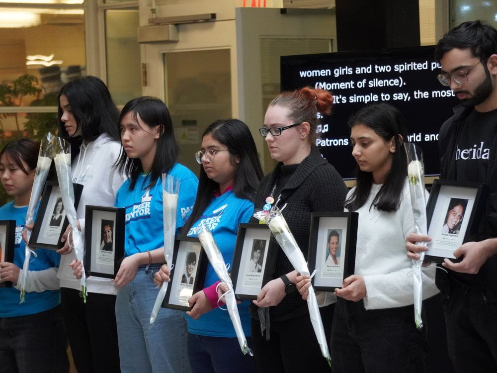 A group of students stands holding framed photos and white roses