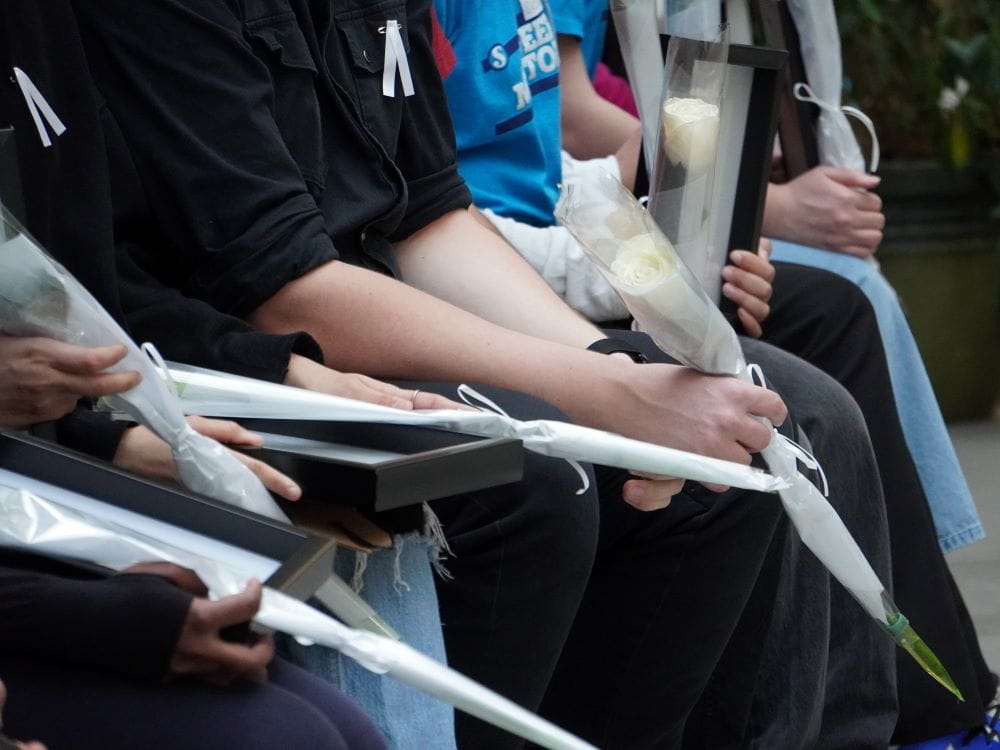 A group of students sitting hold images of women in frames and white roses