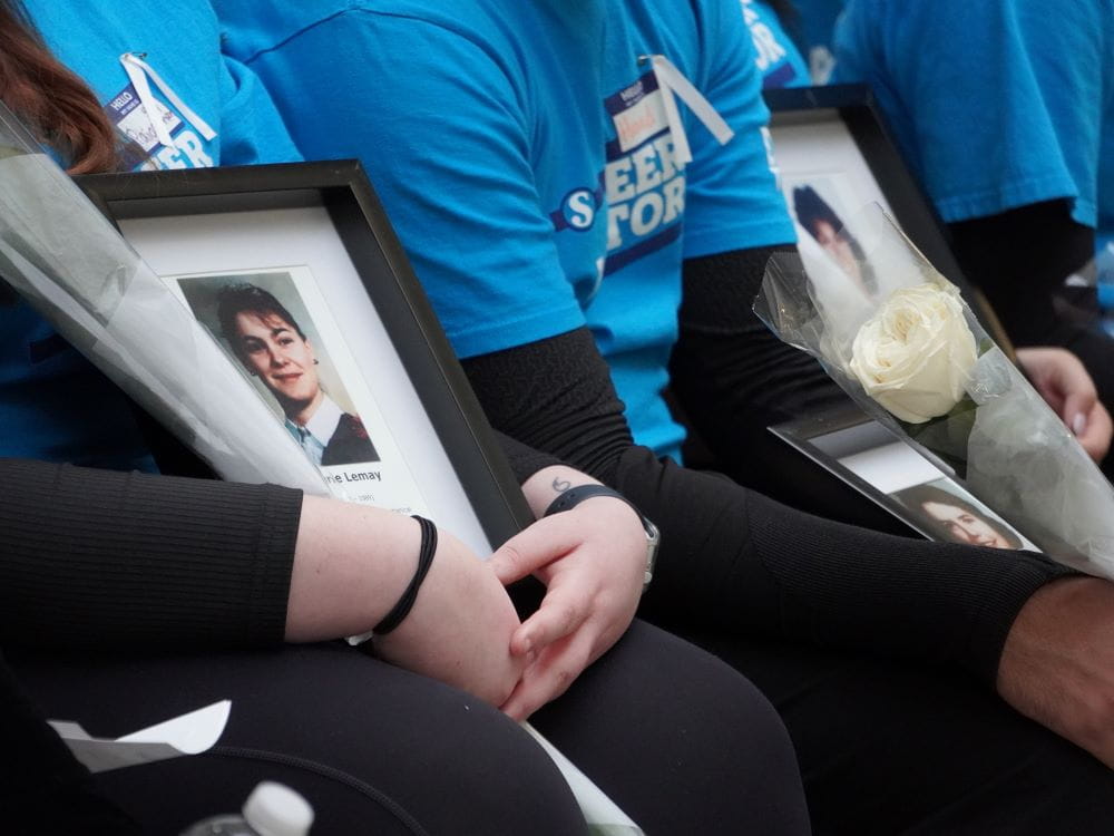 A group of students sitting hold images of women in frames and white roses