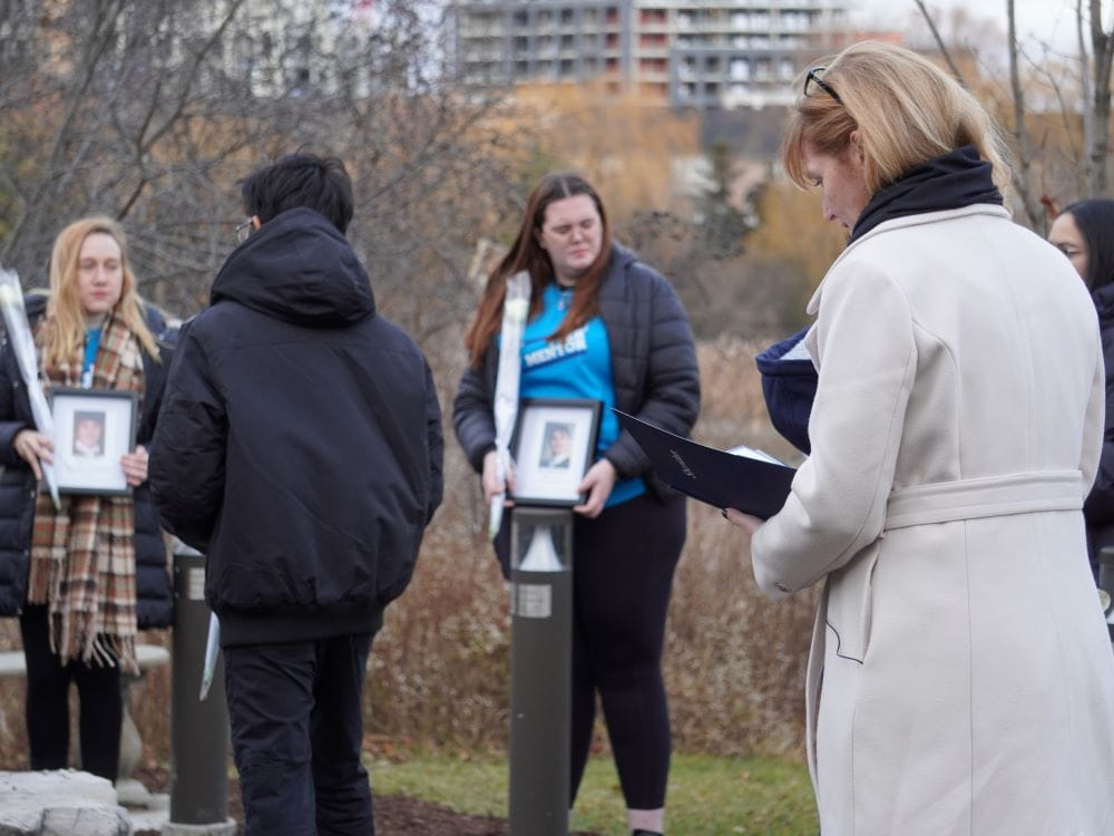 Sheridan's president and students stand in the Davis Campus Peace Garden. Students hold photo frames and white roses.