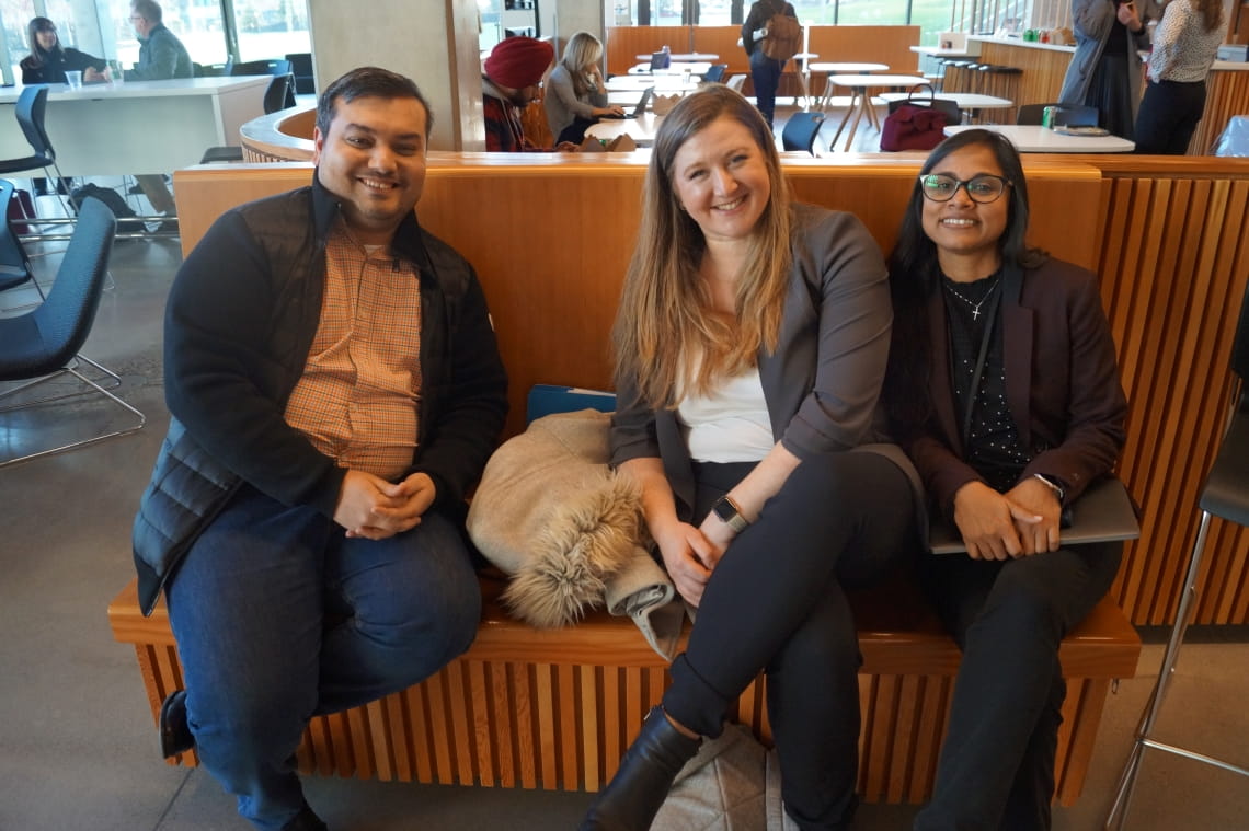Three people are sitting on a wooden bench and smiling at the camera.
