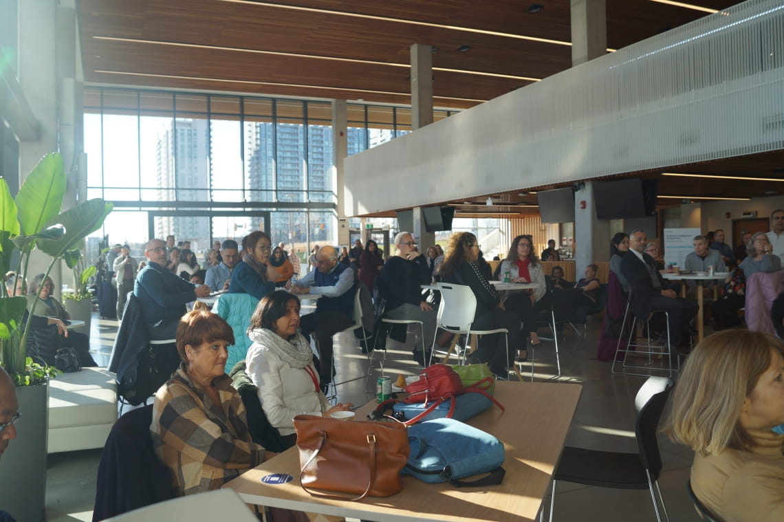 Faculty members listen to a speaker while sitting at tables in the HMC atrium