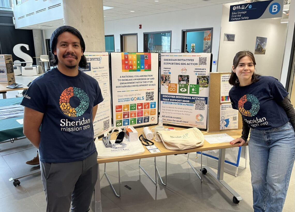 Enrique and Faby stand beside the SDG booth at the networking event