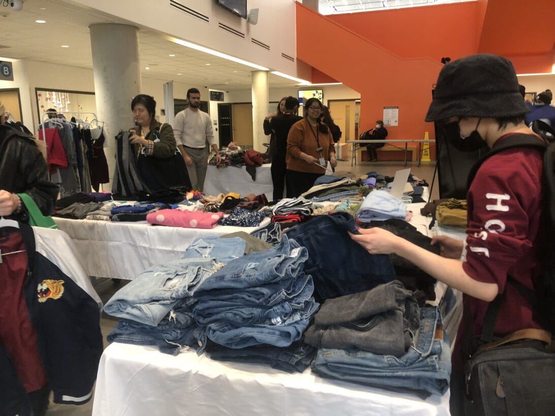 People sort through piles of clothes on tables at the clothing swap
