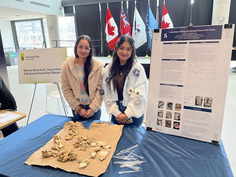 Two students stand at a table with information on mushroom research
