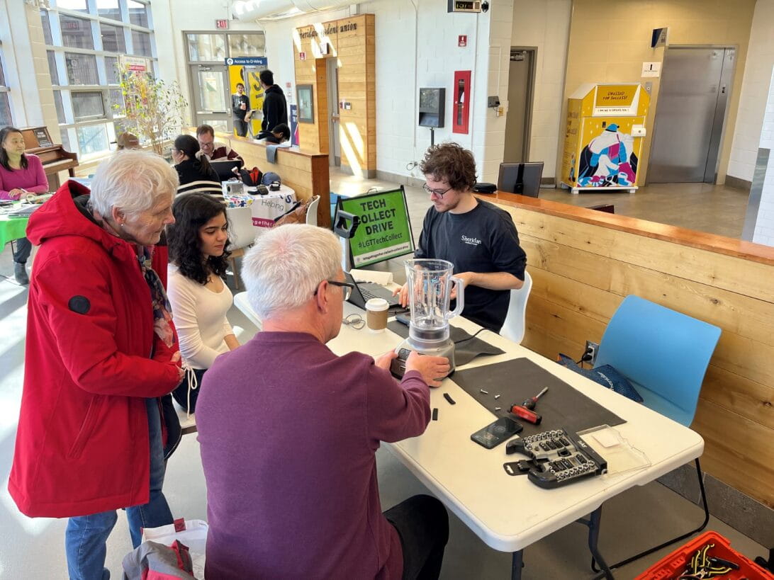 Several people gather around a table of items to be fixed at the repair cafe