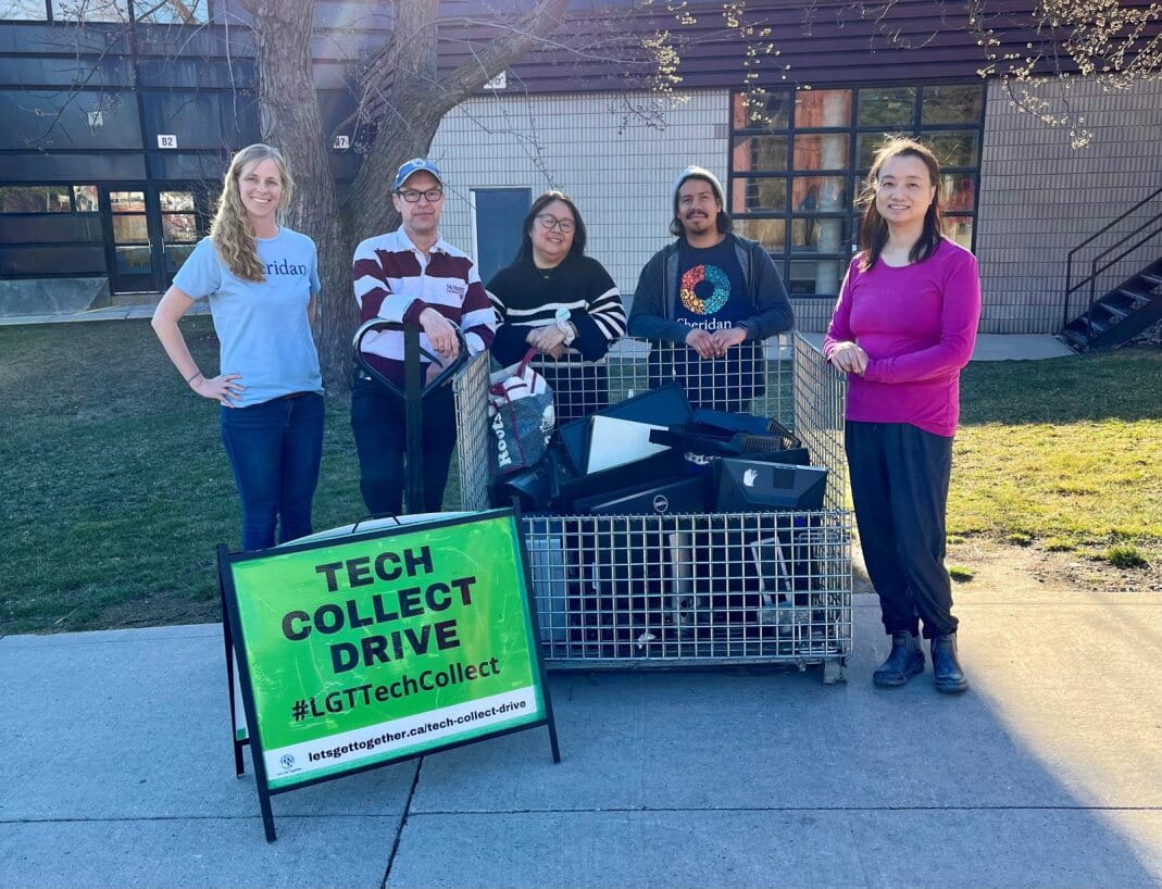 Five people stand outside next to a bin filled with recycled electronics