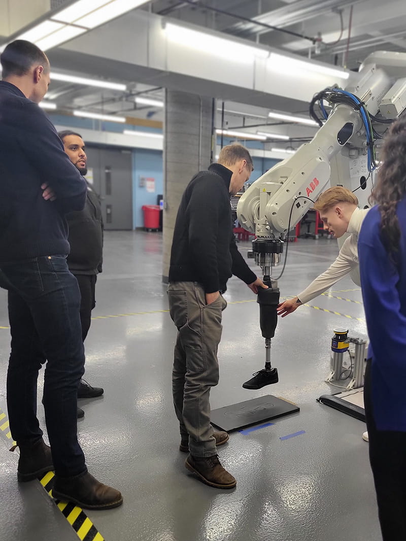 Two people touching a prosthetic leg suspended from a robotic arm