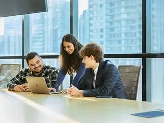 Three students in a conference room looking at a laptop