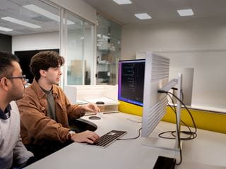 Two students seated in front of two computer monitors
