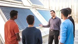 Students and a professor having a discussion while standing in front of solar panels.