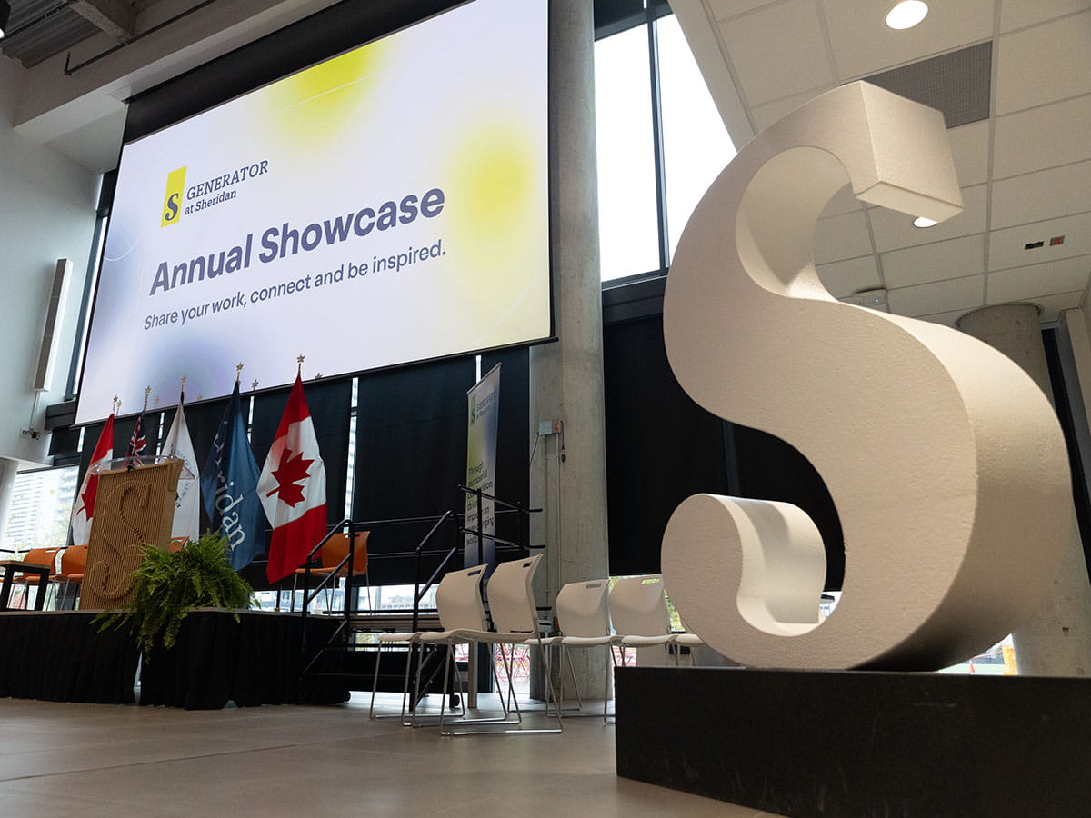 Stage with screen above it reading 'Generator at Sheridan: Annual Showcase. Share your work, connect and be inspired.'