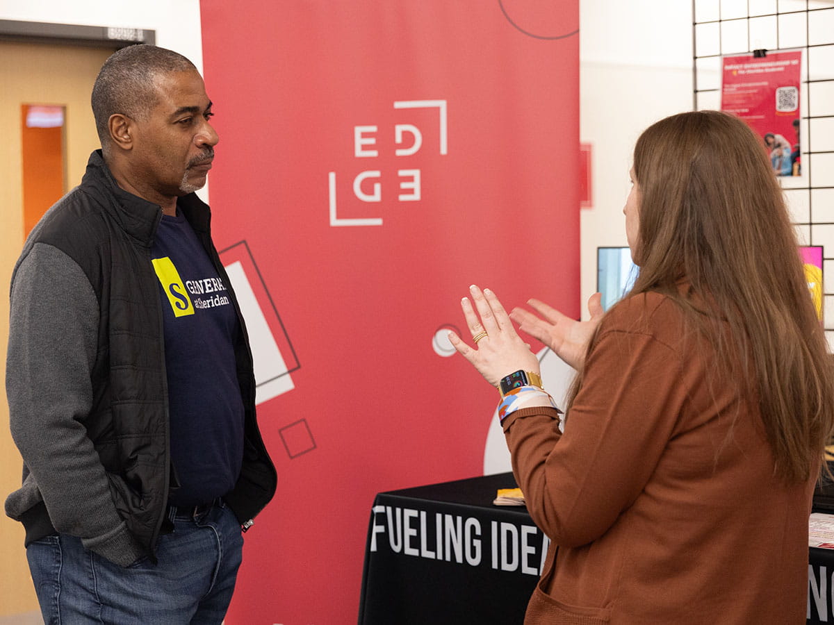 Two people standing and having a discussion. Banner reading 'EDGE' is located between them.