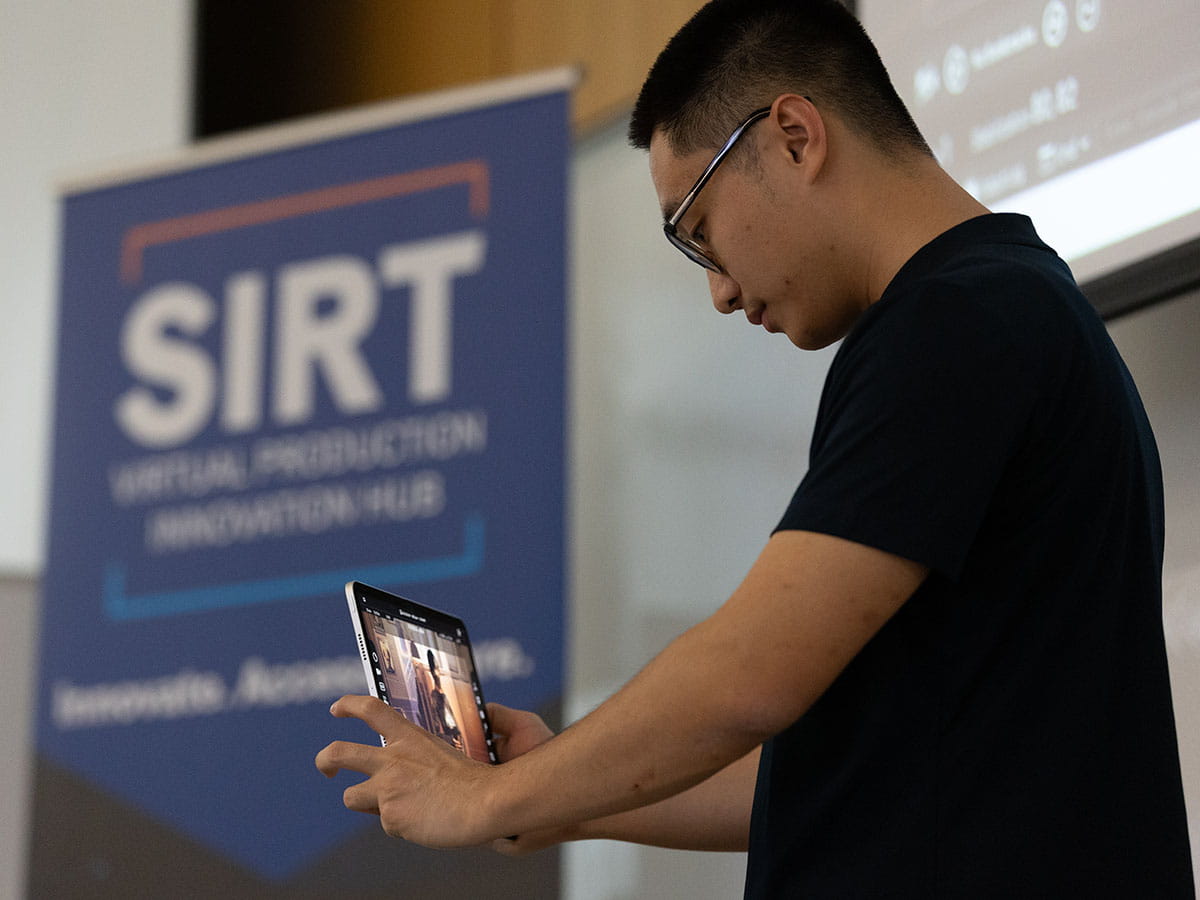 A person interacting with a tablet. A 'SIRT' banner is located behind them and to the left.