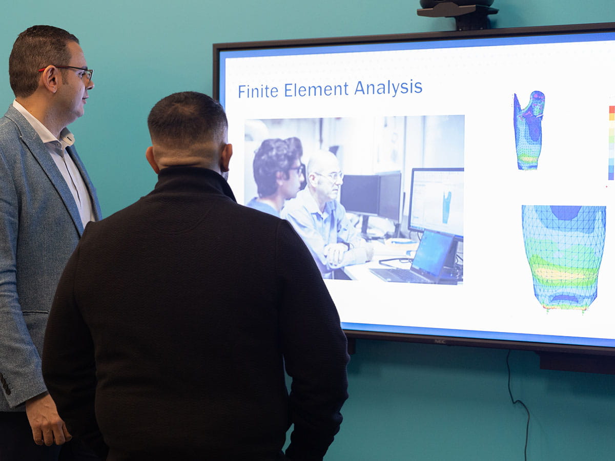 Two people examining a large monitor with a display that reads 'Finite Element Analysis'